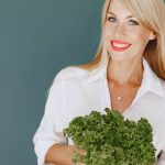 Cheerful woman with blonde hair holding fresh lettuce, promoting healthy living in a studio setting.