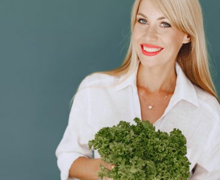 Cheerful woman with blonde hair holding fresh lettuce, promoting healthy living in a studio setting.