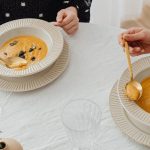 A top view of two people enjoying creamy pumpkin soup with elegant table setting.