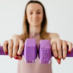 Defocused content young female doing bicep exercise with dumbbells during functional training in light studio