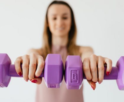 Defocused content young female doing bicep exercise with dumbbells during functional training in light studio